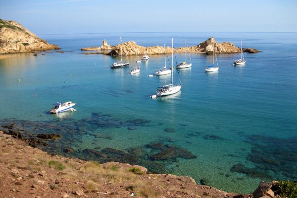 crique à minorque avec une eau turquoise et des voiliers