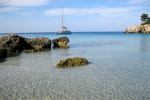 plage avec une eau bleu transparente et un catamaran blanc