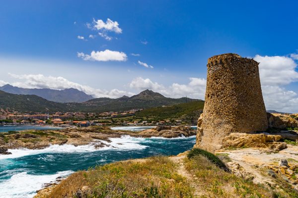 une tour de pierre au bord de la mer et un village au loin